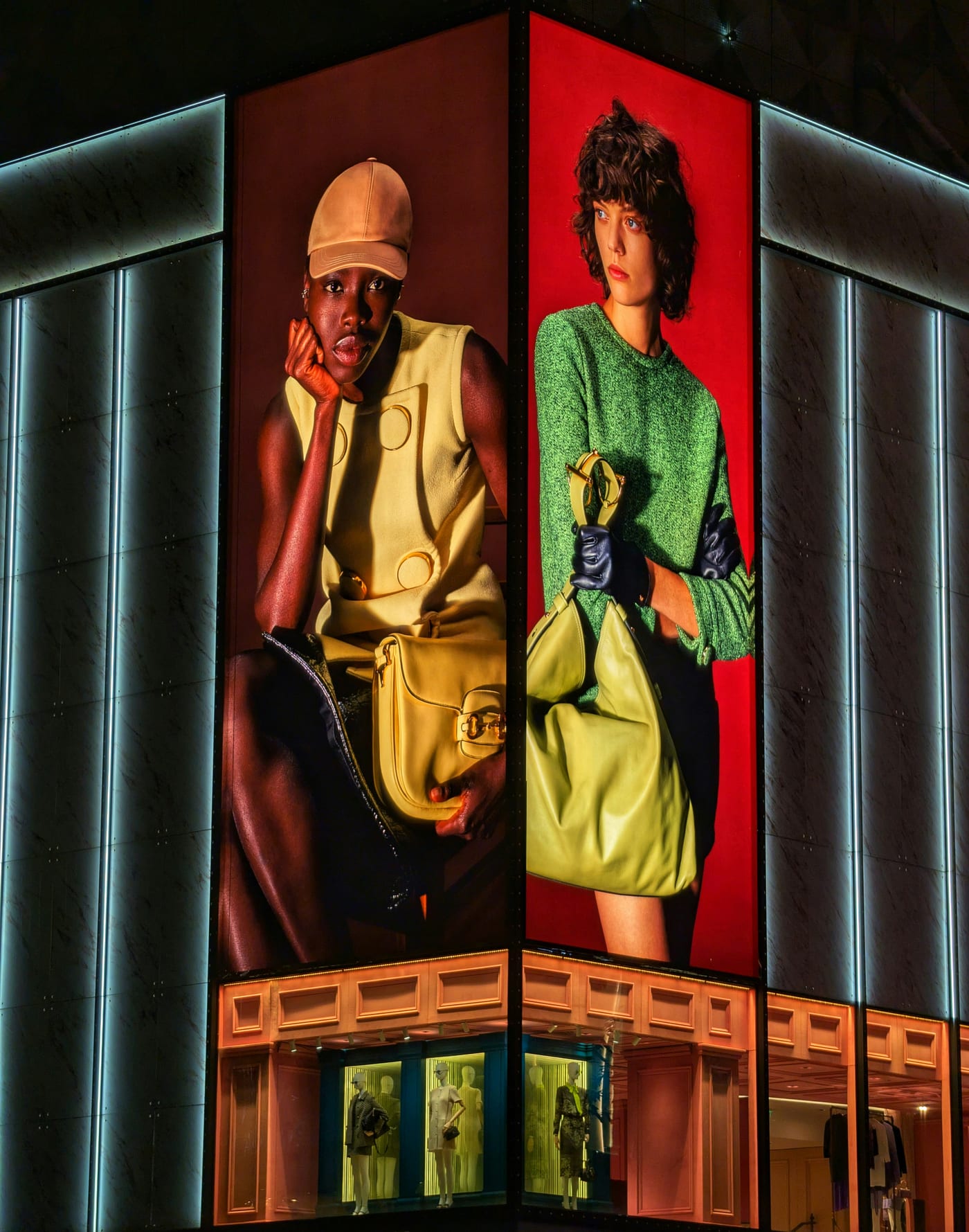Two illuminated fashion campaign posters wrapping the corner of a store facade at night