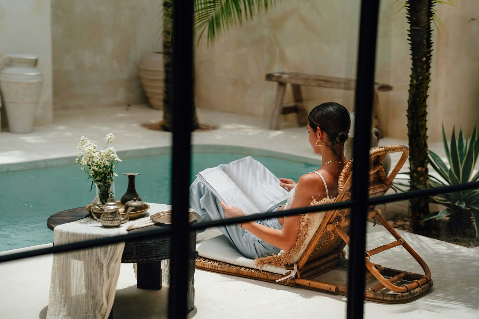 A woman reading in a rattan chair beside a courtyard pool, shaded by palms