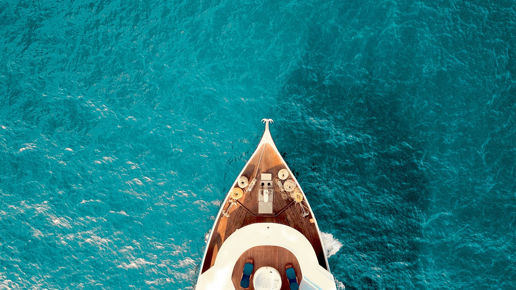 Aerial view of the bow of a white yacht cutting through clear turquoise sea
